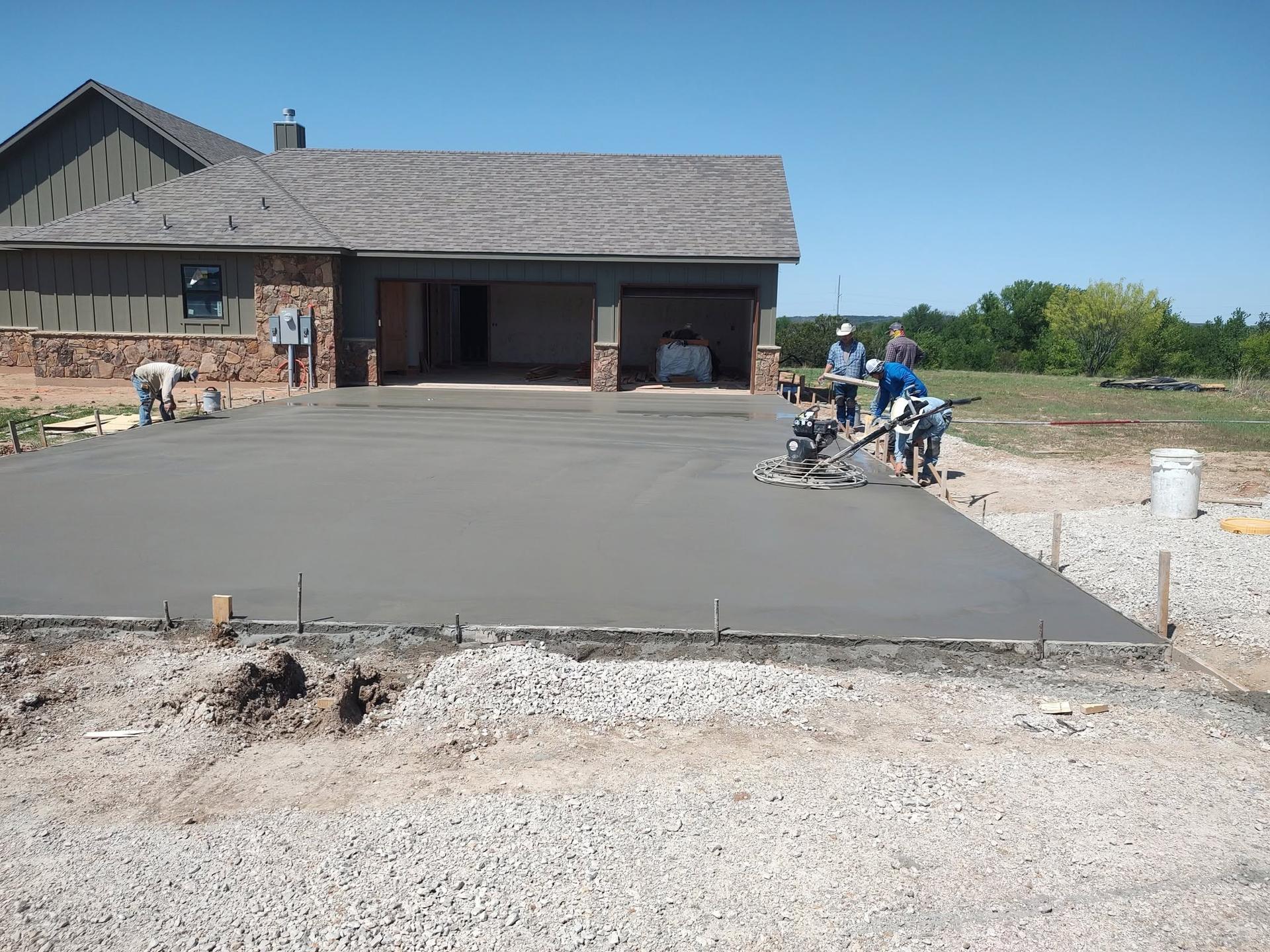Crew finishing a freshly poured concrete driveway apron in front of a home's garage with a power trowel machine