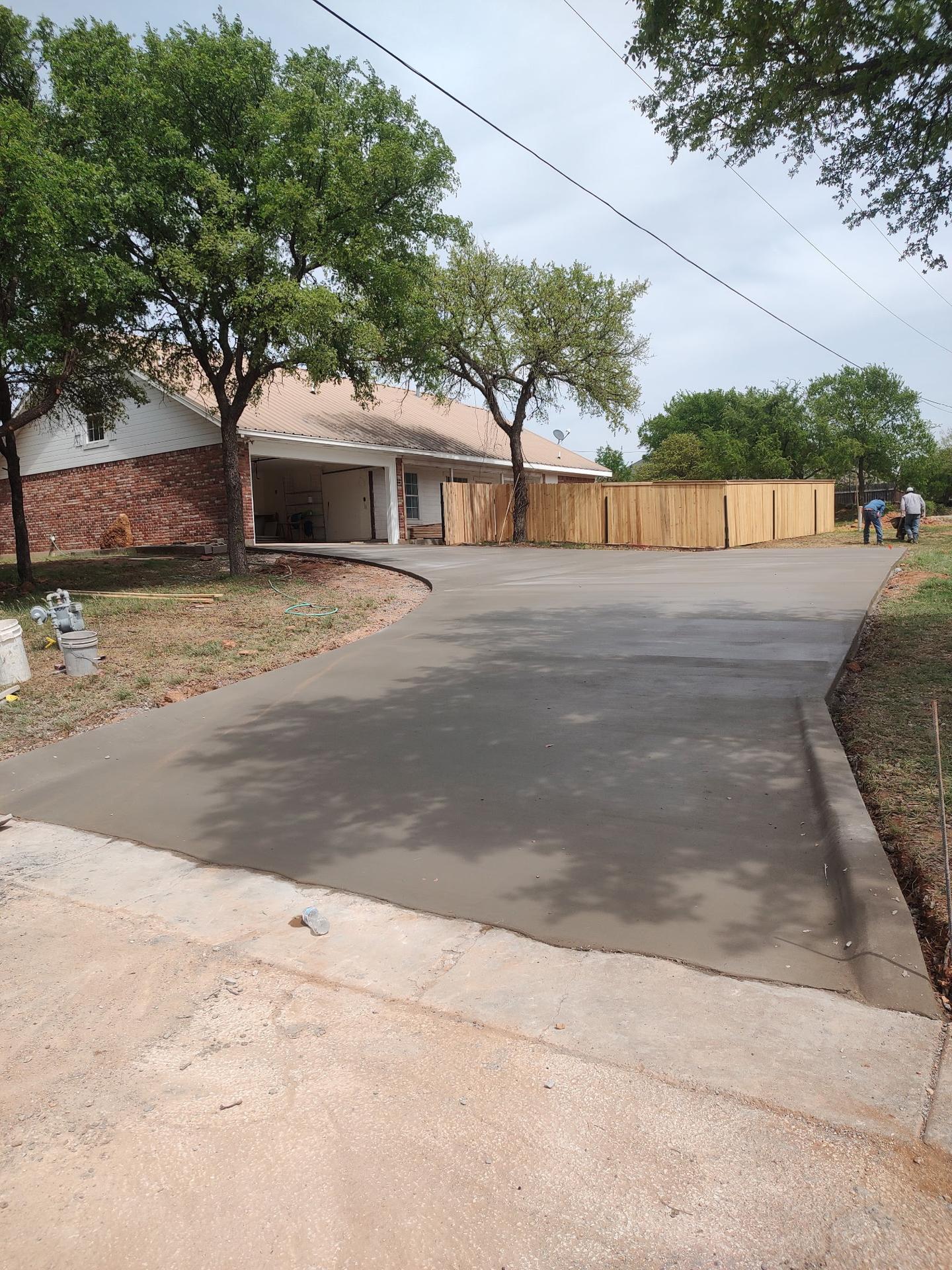 Newly poured curving concrete driveway leading to a brick home's garage, with a new cedar privacy fence along the side