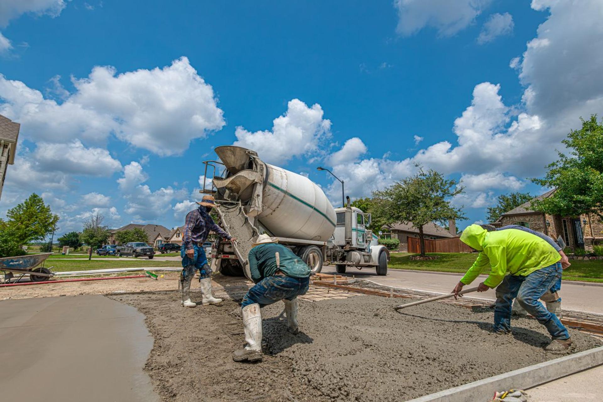 Crew pouring and finishing a residential concrete driveway with a ready-mix truck parked on the street