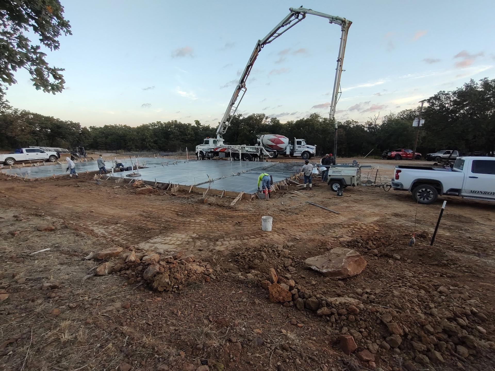 Freshly poured concrete slab with the pump truck boom overhead and crew finishing the edges at dusk