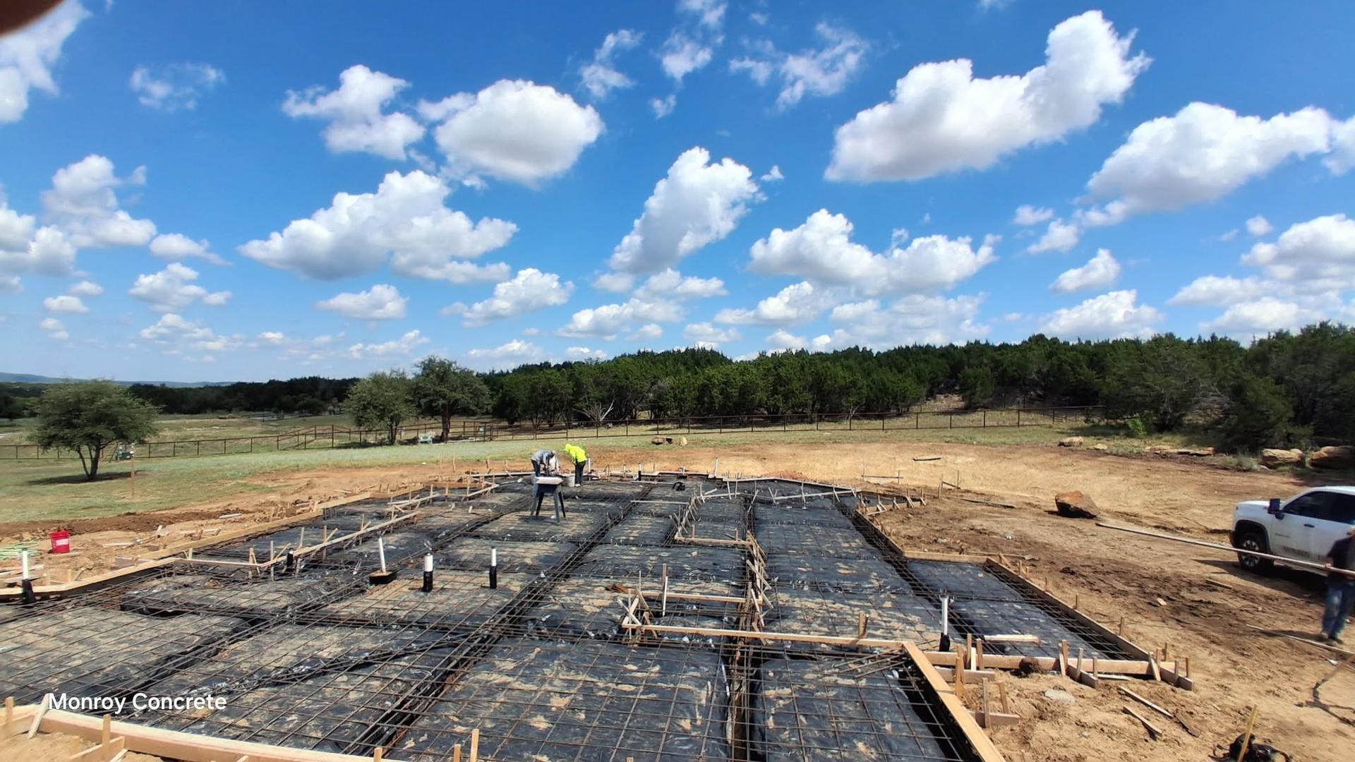 Wide view of a large rebar-reinforced foundation grid laid out in a rural field before the pour