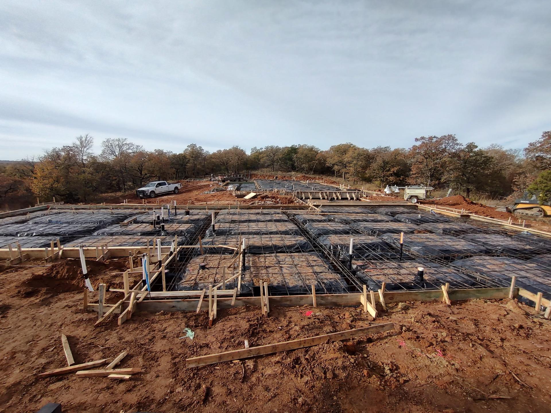 Poured concrete foundation wall with a rebar-reinforced slab grid staged in front of it, ready for the next pour