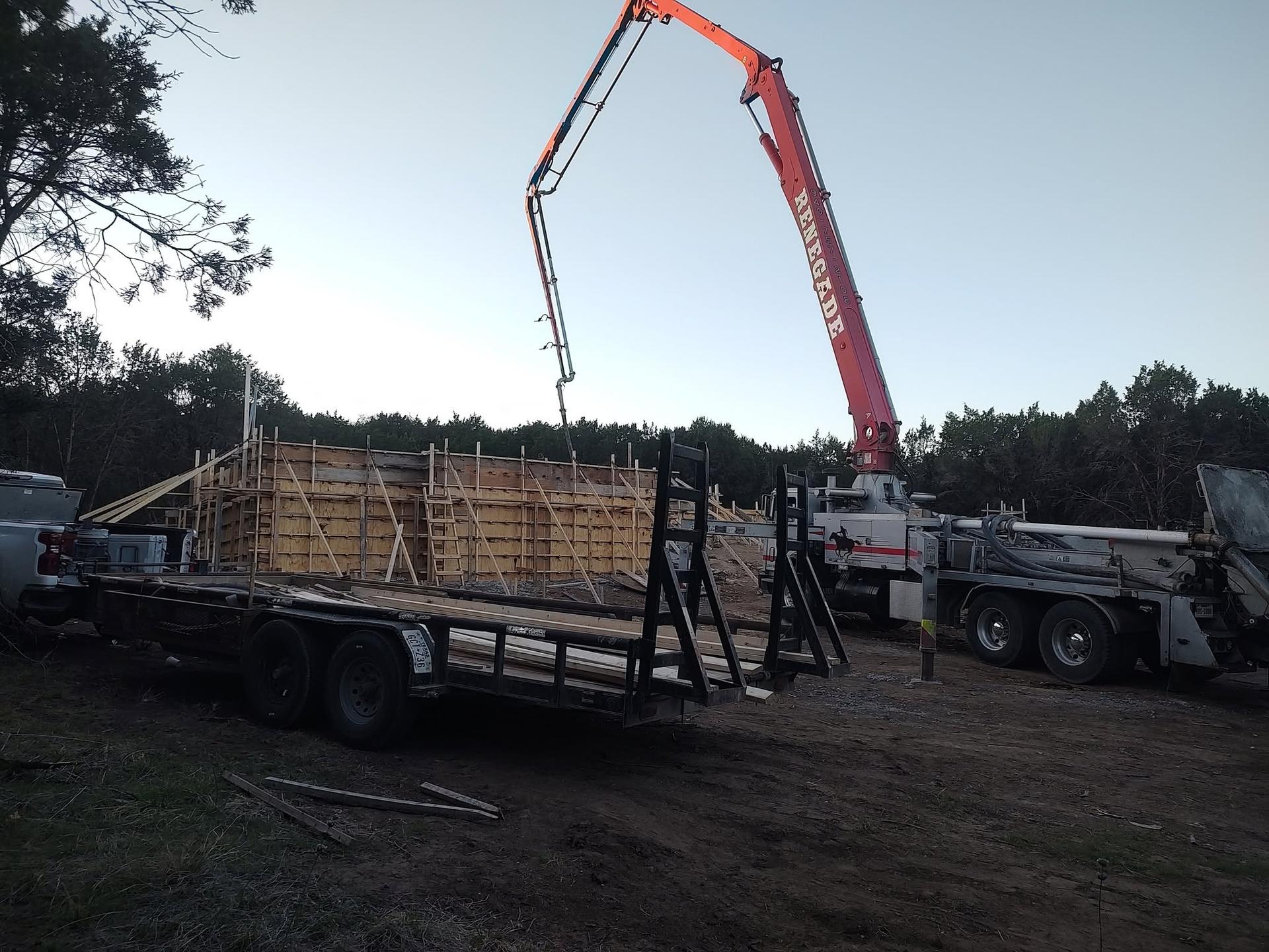 Concrete pump truck boom extended over wood formwork to pour a wall at dusk