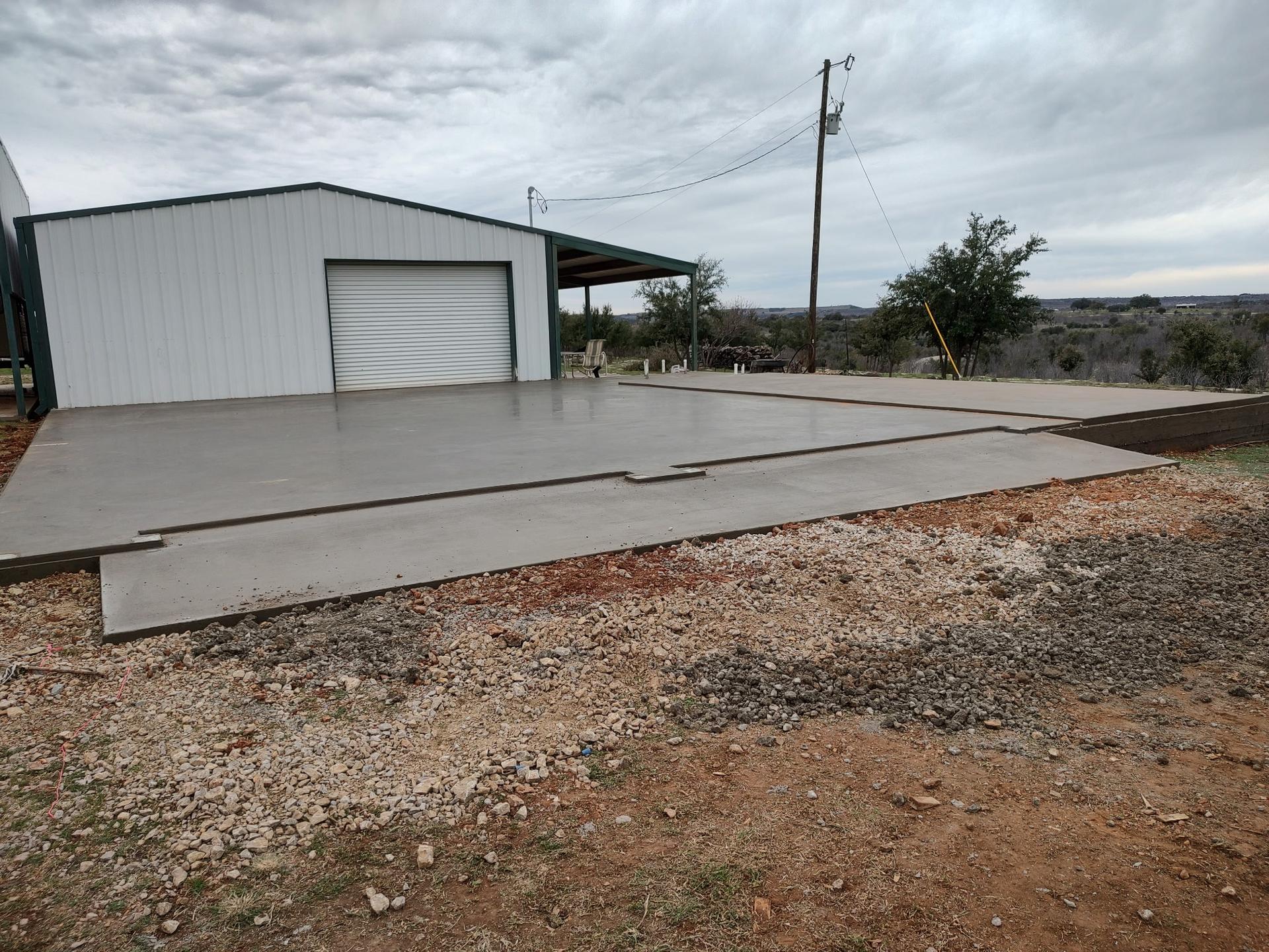 Finished concrete slab in front of a metal shop building with an attached carport, ready for use
