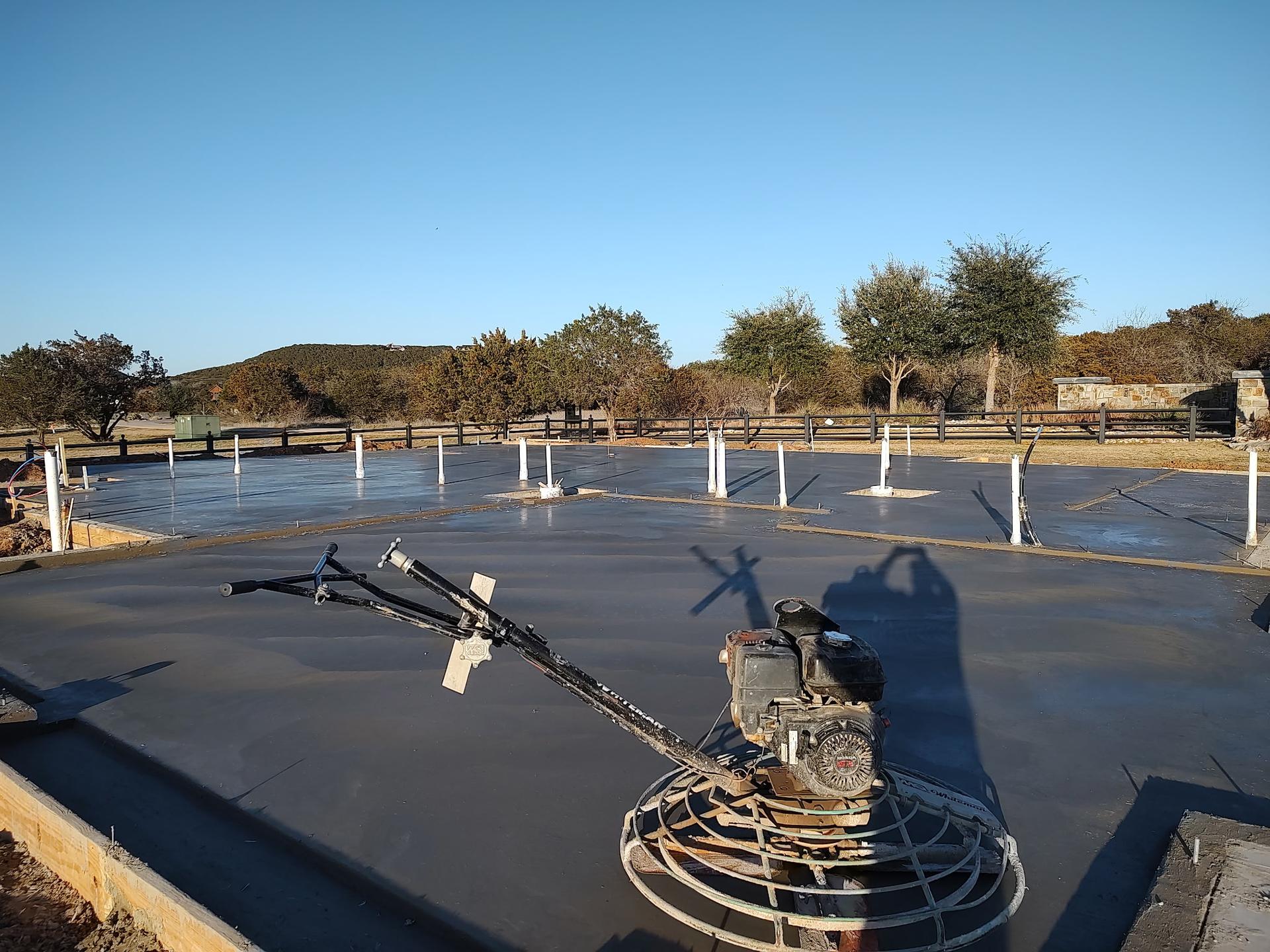 Freshly finished concrete slab on a rural building site with a power trowel machine and open land beyond