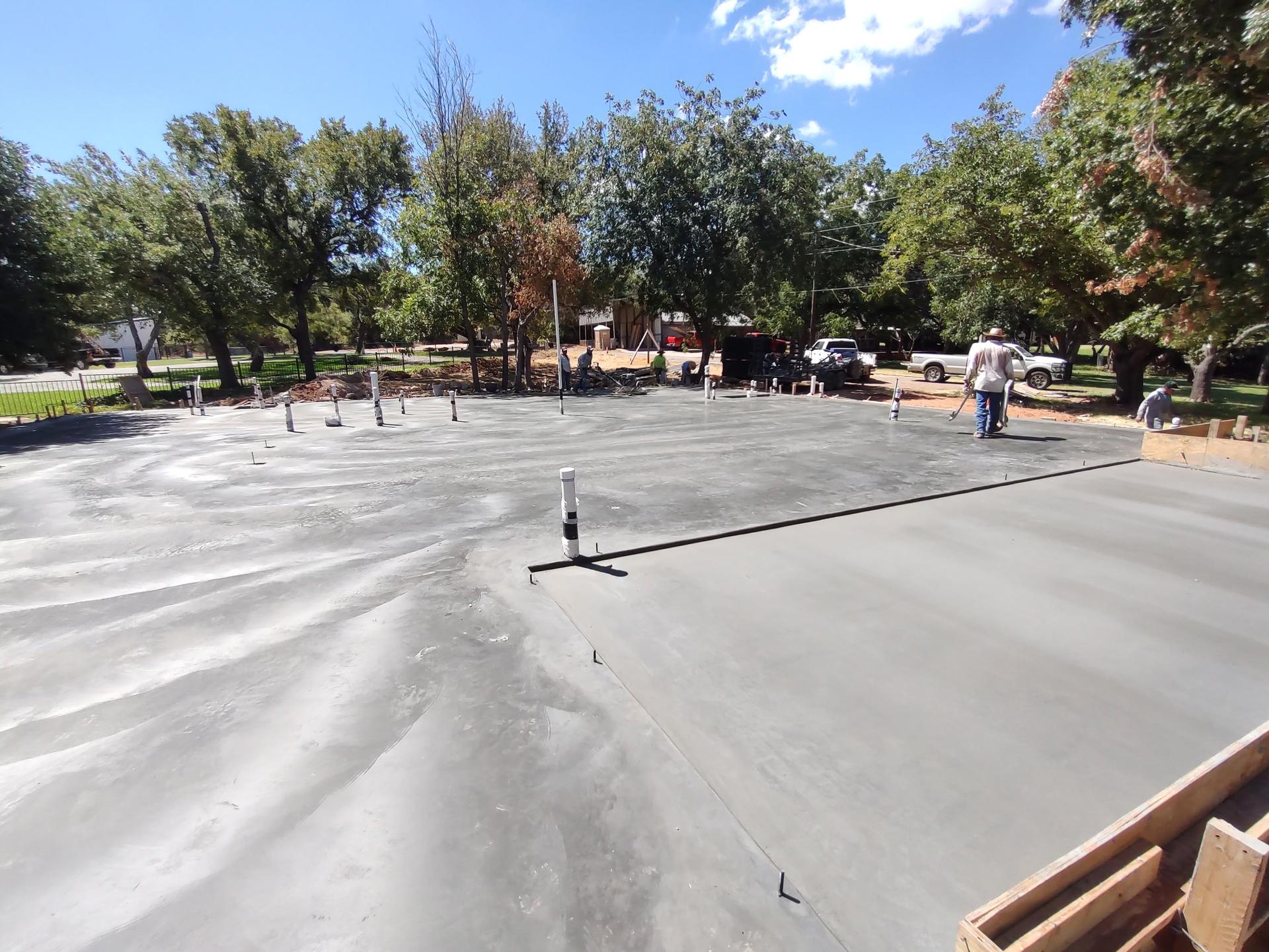 Large finished concrete slab with a power trowel machine parked on it and crew walking the surface